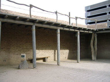 A view of a loggia’s inside corner with adobe brick walls and log posts.