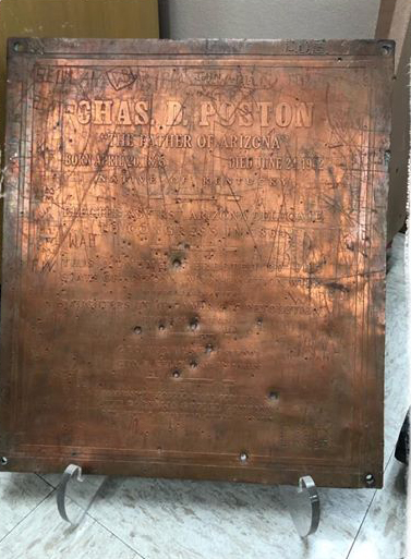 A snapshot of a copper plaque with text; surface is damaged. Is in a display stand.