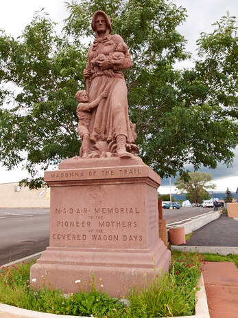 A snapshot of a statue of a woman holding a baby with a young child clinging to her skirts, a Madonna of the Trail.