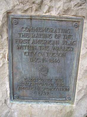 An historical plaque mounted on a stone that reads, “Commemorating the Raising of the First American Flag within the Walled City of Tucson / Dec. 16 1846 / Erected by the Daughters of the American Revolution / 1939”. Former Spanish Presidio.