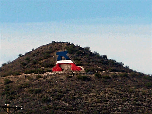 A snapshot of a rounded hilltop with a large red, white, and blue “A” on the ground.