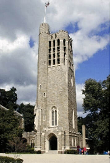 A narrow, grey stone tower, several stories high, with an arched doorway and openwork at the top showing bells. It contains the Arizona Bell Valley Forge.