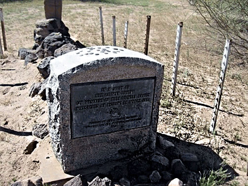 A snapshot of a marker with plaque. A wire fence appears to surround the area.