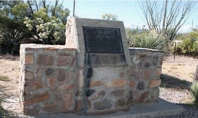 A snapshot of a concrete and stone marker in the mid-ground of a desert setting.