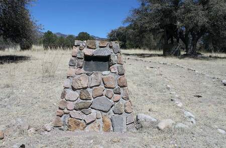 A snapshot of the concrete and stone marker with plaque in a scrubland setting.