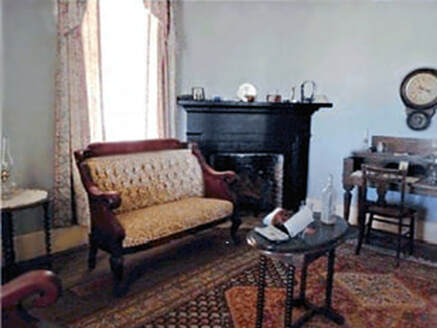 A snapshot of the interior of the customs house with period furnishing, including a rug, settee, fireplace, desk with chair, and clock.