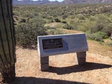 A snapshot of a marker with plaque in a desert setting with mountains in the background. Marks the Stoneman military trail.