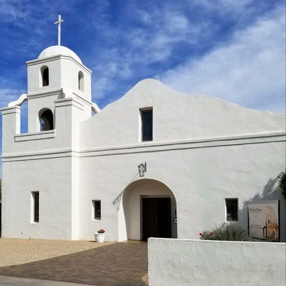 A photograph of a white church building in the Southwest style, called the old adobe mission.