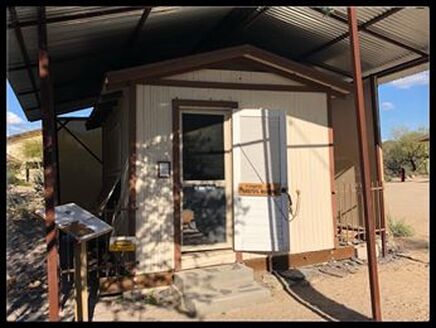 Snapshot of a one-room cabin, perhaps 10-feet by 10-feet, painted, under a protective roof.