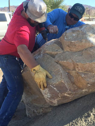 A snapshot of two workers moving a large boulder into place