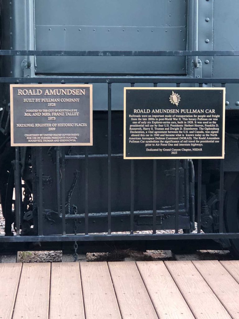 A snapshot of two markers, side by side, mounted on a railing. The marker on the left acknowledges the gift of the Pullman Car (1973) and its inclusion on the National Register of Historical Places (2009). The marker on the right is the DAR marker. Marker text is in the body of this page.