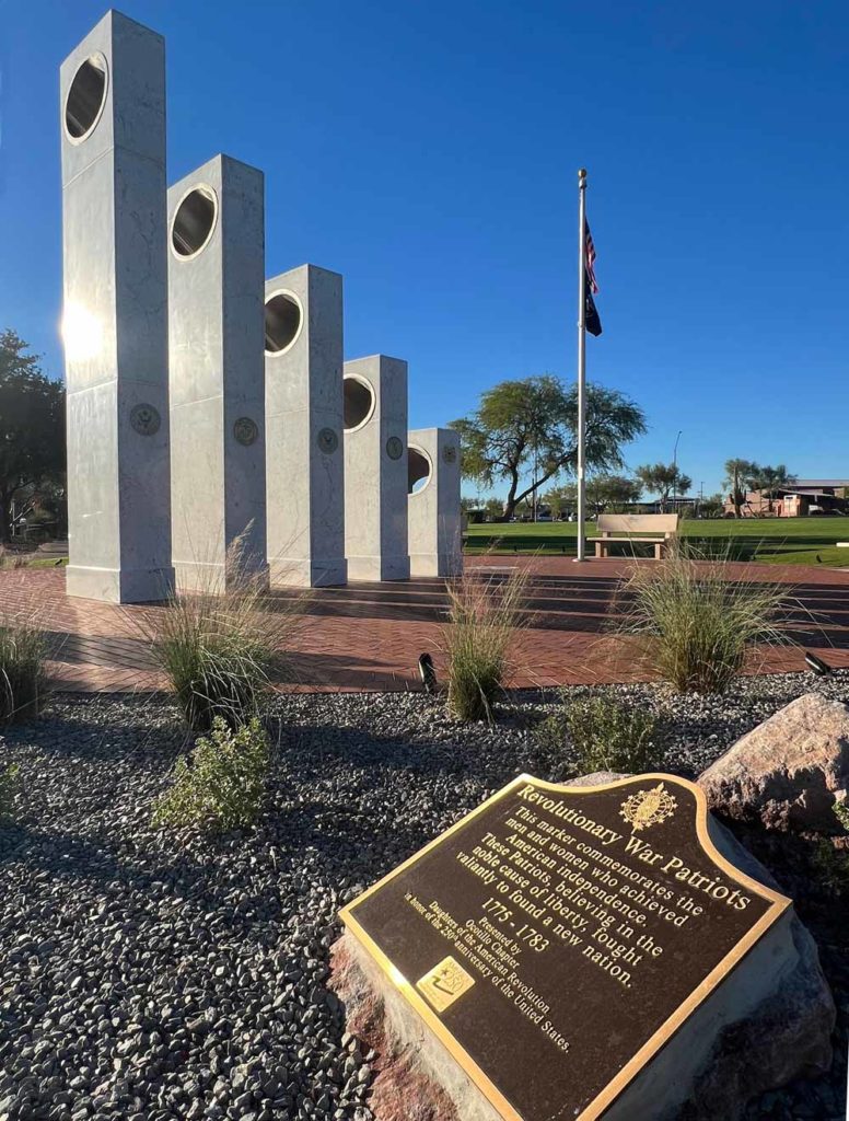 A snapshot of the marker with five pillars and the flagpole of the memorial plaza in the background.