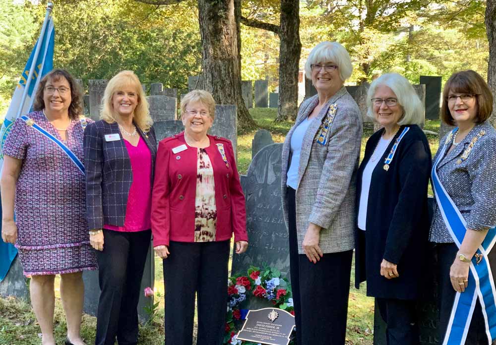 A snapshot of six women standing beside the grave and marker.