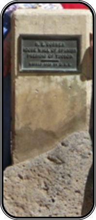 A blurry snapshot of the bronze plaque affixed to a smooth concrete marker embedded in a piece of broken concrete.