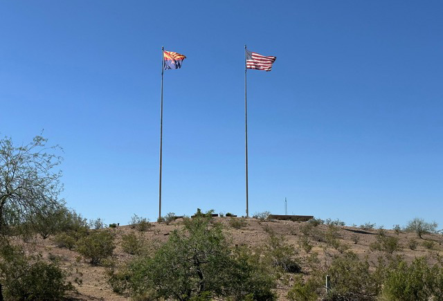 A snapshot of a desert rise with two flagpoles silhouetted against the sky.