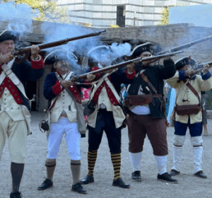 A photo showing five men dressed as Revolutionary and Presidio soldiers while firing muskets.